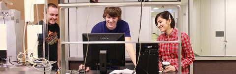 A group of three students gathered in a lab room, focusing on a computer screen.