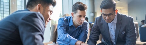 Three students in shirts and suit jackets work at a low table