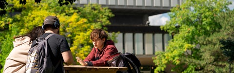 Students sitting a table with trees and building in background