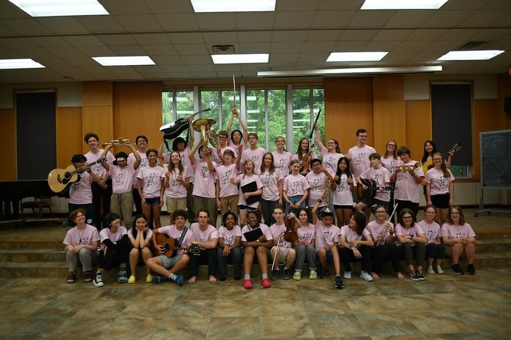 Large group of young students wearing pink OMMC shirts, posing with instruments, and smiling at the camera